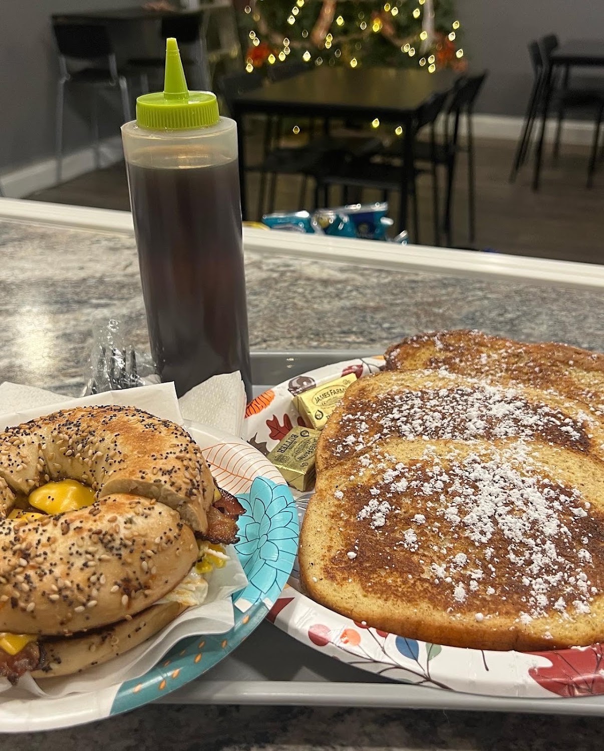 An everything bagel sandwich with bacon and egg beside thick cut French toast dusted with powdered sugar.